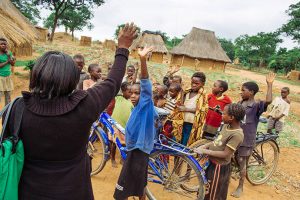 Racheal Mokosha, District Malaria Focal Person, stands in front of a crowd of children in Harmony village.