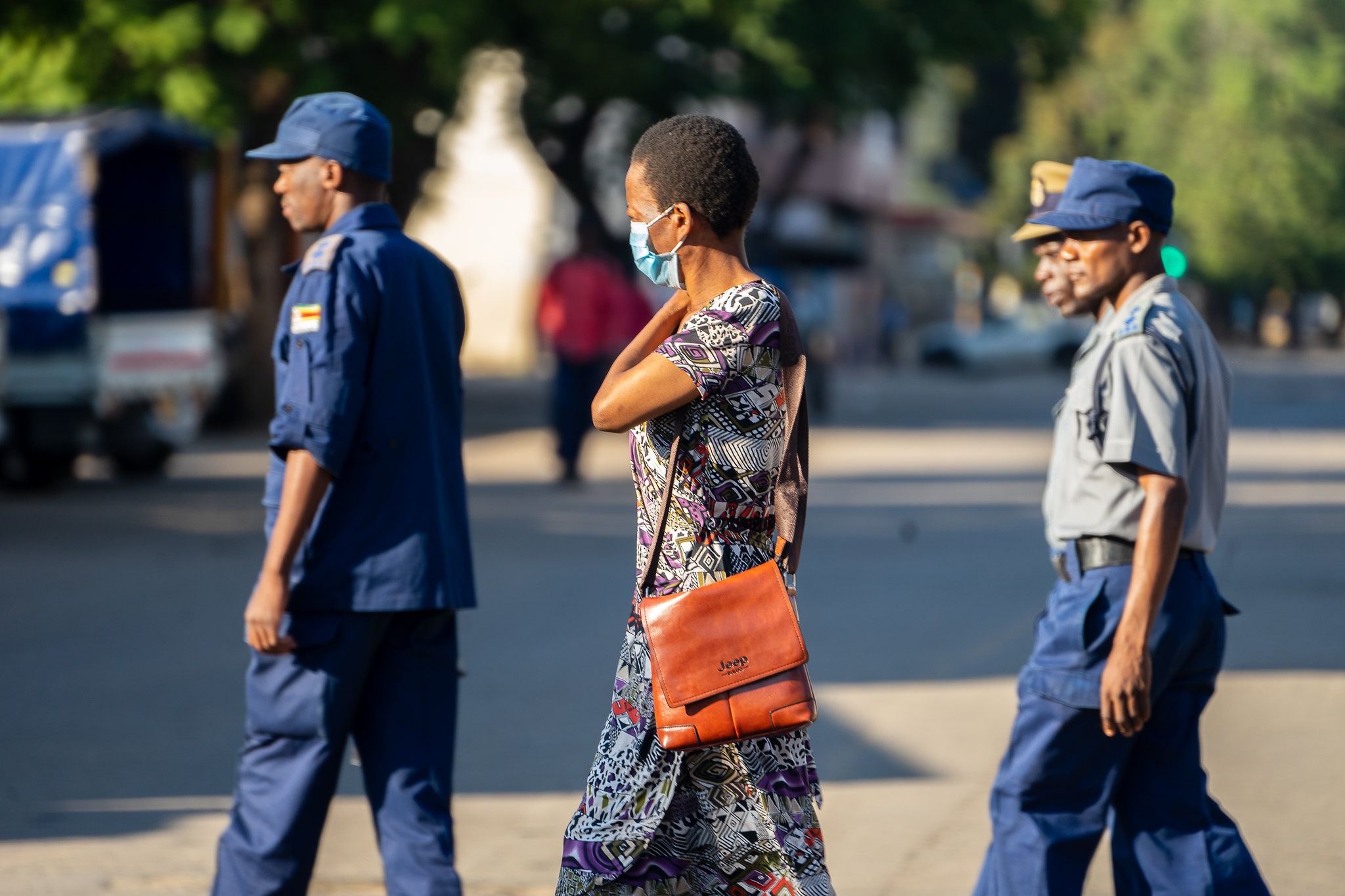 Harare, Zimbabwe. A woman wearing a COVID-19 protective mask walks past a group of police officers on patrol in Bulawayo CBD, 1 April 2020. Photo credit: KB Mpofu / ILO (CC BY-NC-ND 2.0)