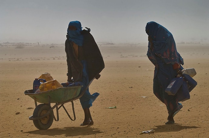 View of two refugees walking in the wind with wheelbarrow